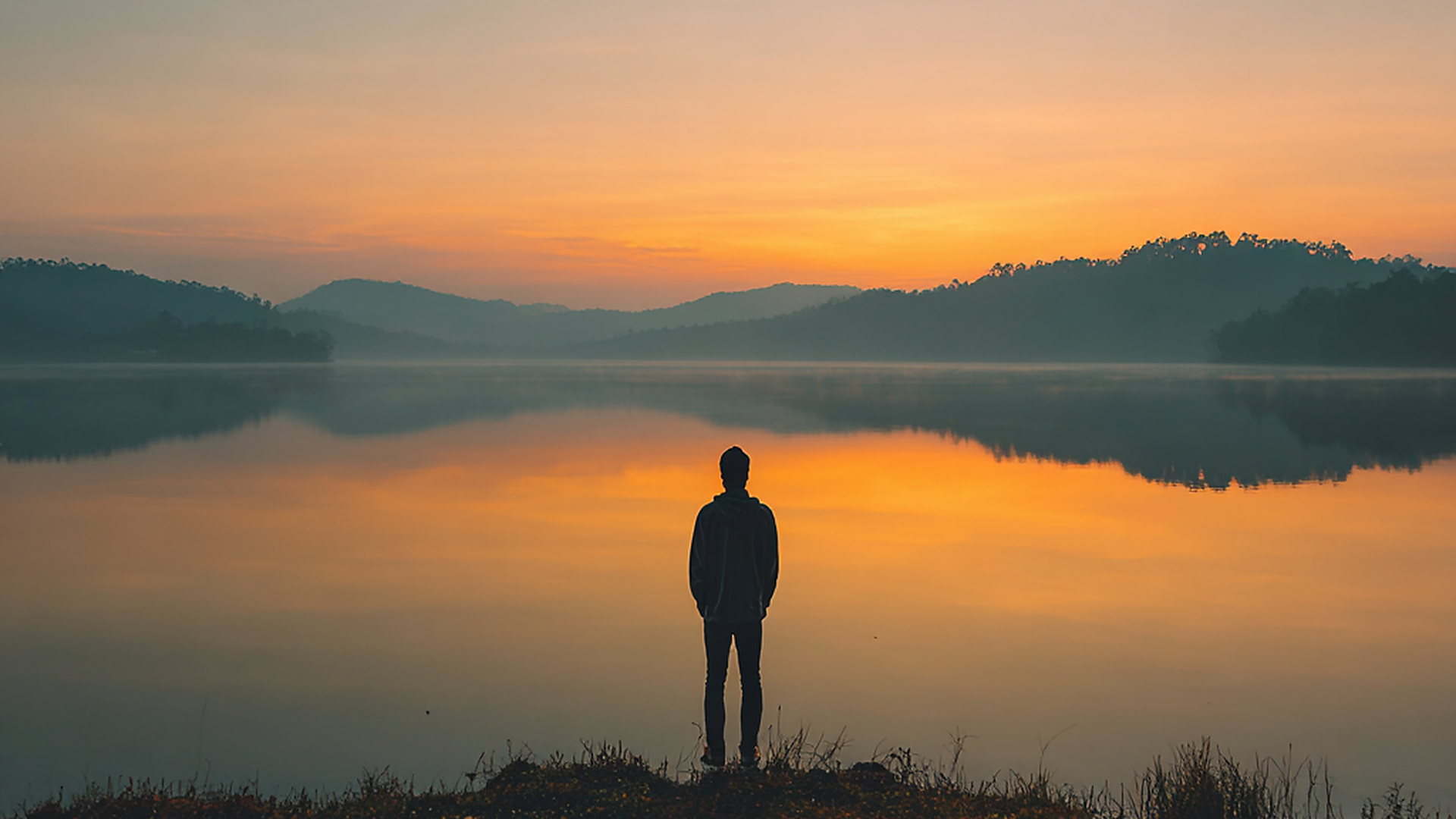 A person standing quietly at a lake at sunrise